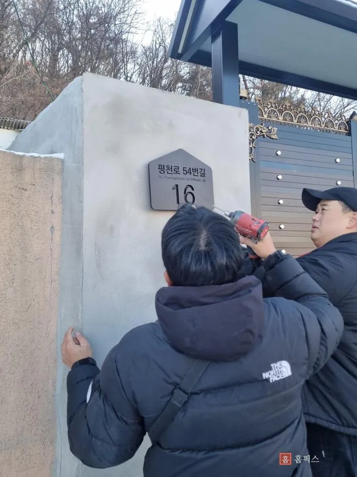 기둥에 도로명주소판을 대고 전동드릴로 고정하는 작업자 두 명