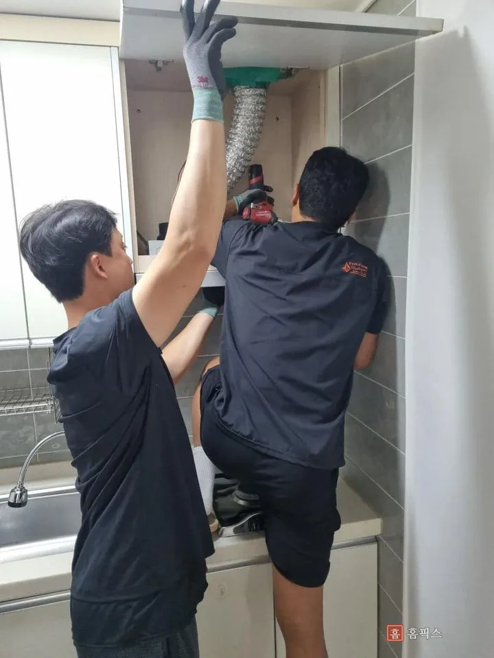 후드장 안에서 주름관을 연결하고 본체를 고정하는 작업자 두 명