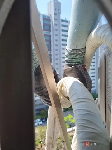 난간 사이로 끌어온 배관의 해진 테이프를 가위로 잘라내는 모습