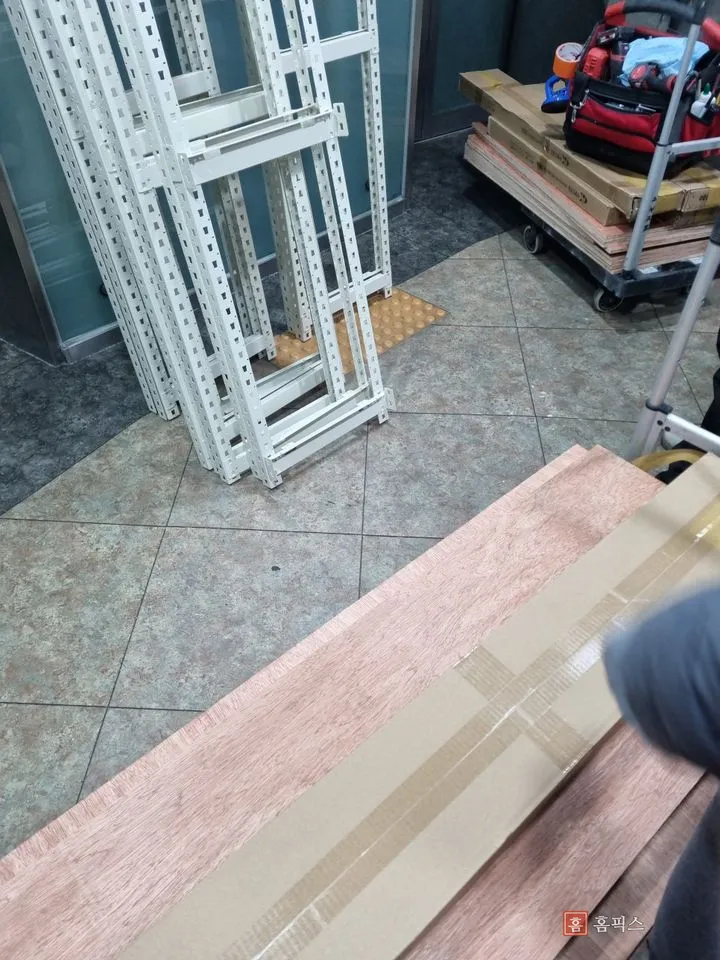 건물 로비에 내려놓은 앵글 프레임과 목재 상판, 공구 수레